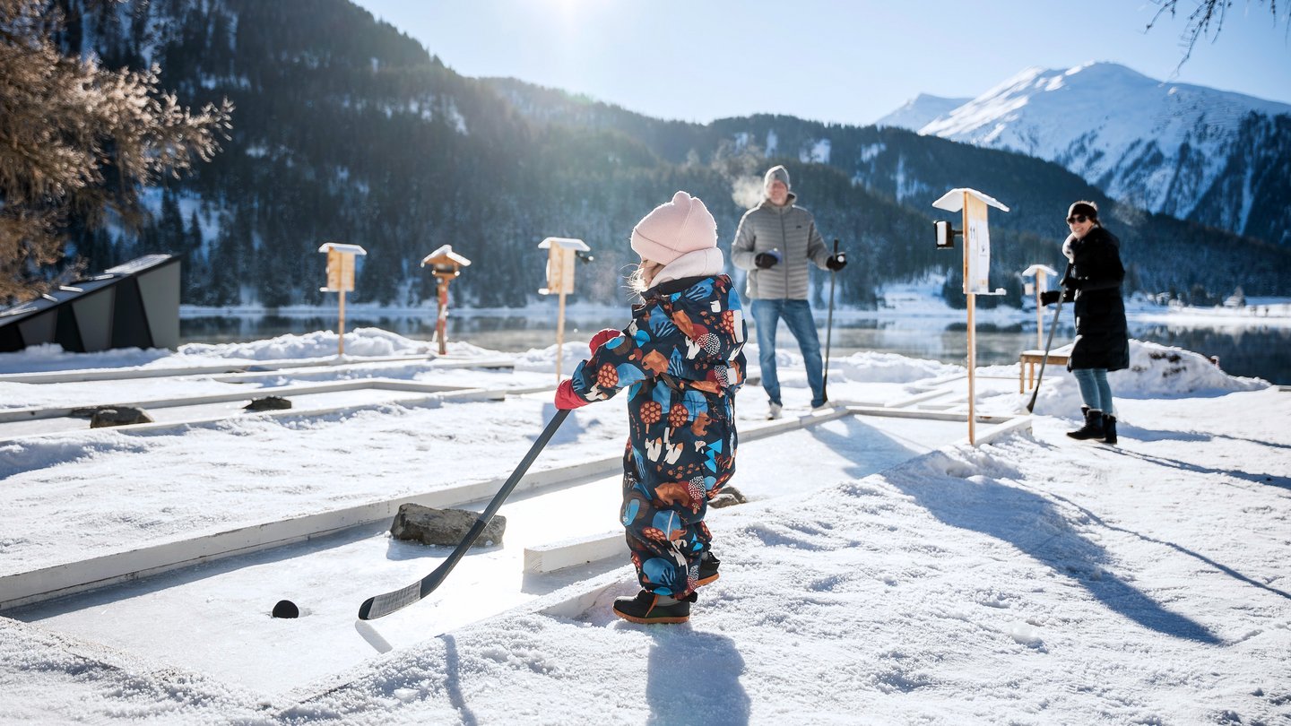 Eis-Minigolf spielen am Davosersee mit Hockeyschläger und Puck.